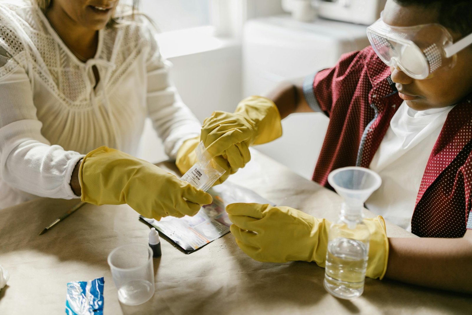 A mother and child conducting a science experiment with gloves and goggles indoors.